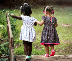 Two little girls stroll together across a bridge, enjoying a sunny day in a natural setting.