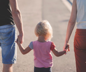 A young girl joyfully holds hands with her parents, symbolizing family unity and love.