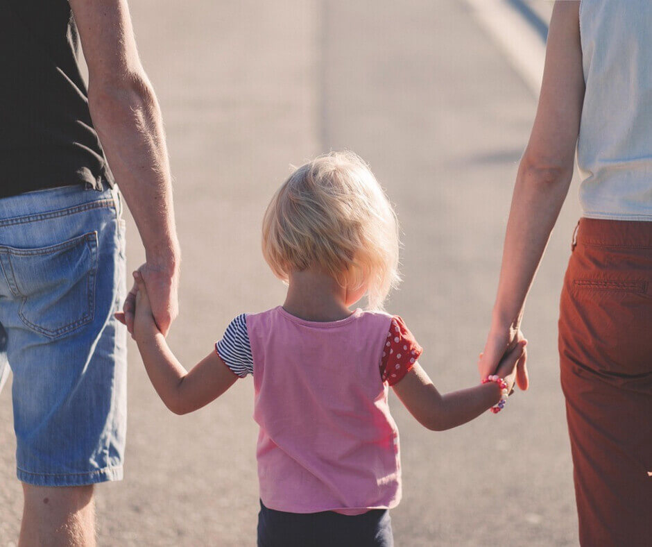 A young girl joyfully holds hands with her parents, symbolizing family unity and love.