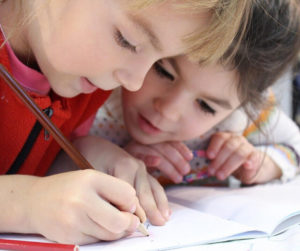 Two young girls are engaged in writing in a notebook, sharing ideas and concentrating on their work.