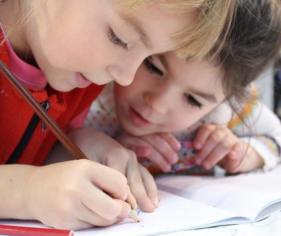 Two young girls are engaged in writing in a notebook, sharing ideas and concentrating on their work.