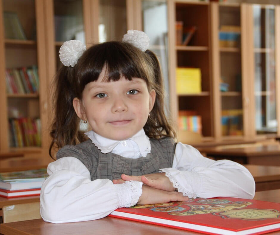 A young girl sits at a desk, focused on reading a book, surrounded by colorful stationery.