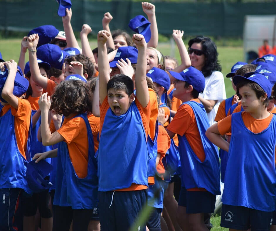 A group of children wearing blue and orange shirts and hats, smiling and playing together outdoors