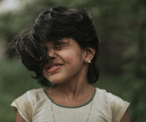 A young girl with wind-swept hair smiles, embodying a sense of adventure and playfulness in an outdoor setting.