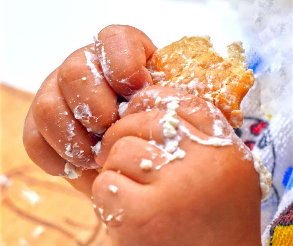 A small hand holding a piece of dough, indicating a child's involvement in cooking or baking activities.