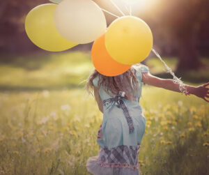 A cheerful girl dashes through a green field, clutching a bunch of bright balloons, radiating joy and freedom.