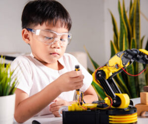 A young boy is focused on assembling a robot, surrounded by tools and parts on a workbench.