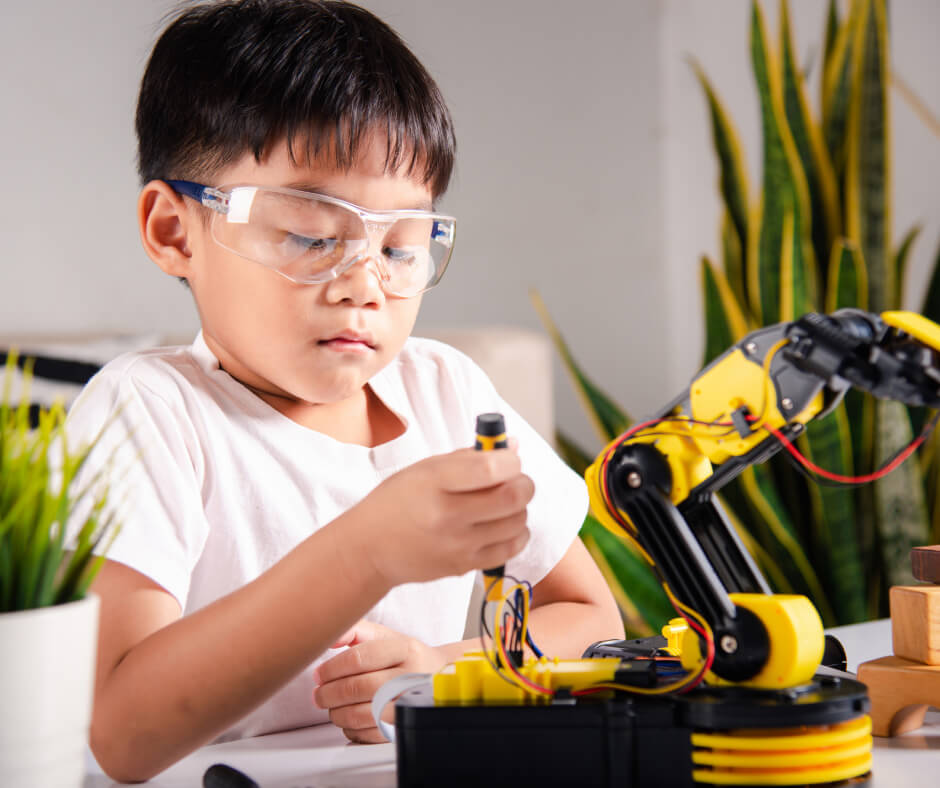 A young boy is focused on assembling a robot, surrounded by tools and parts on a workbench.
