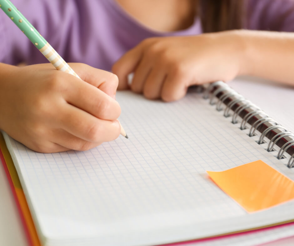 A child focused on writing in a notebook with a pencil, showcasing concentration and creativity.