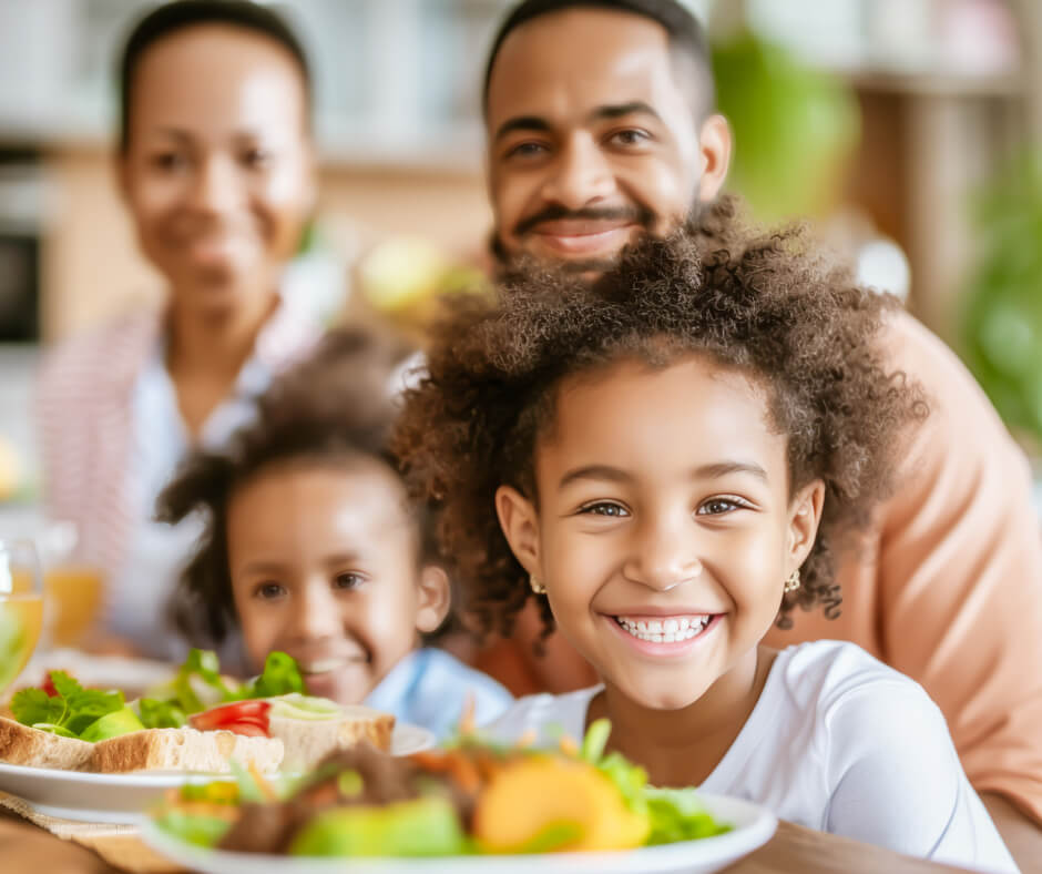 A family shares a joyful moment, smiling as they eat a meal together at home.