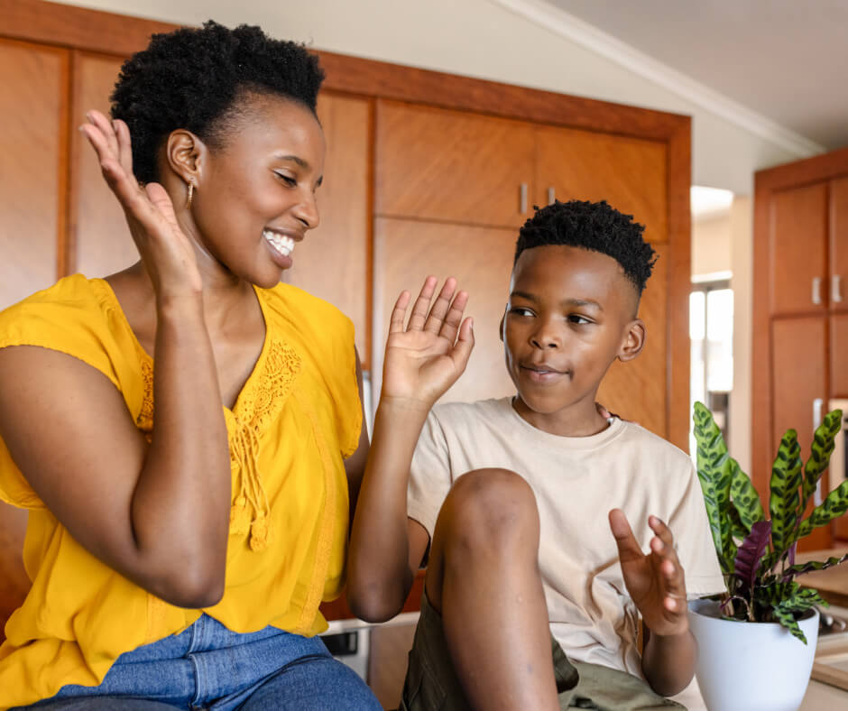 A woman and a boy sit together on a kitchen counter, sharing a moment in a cozy home environment.