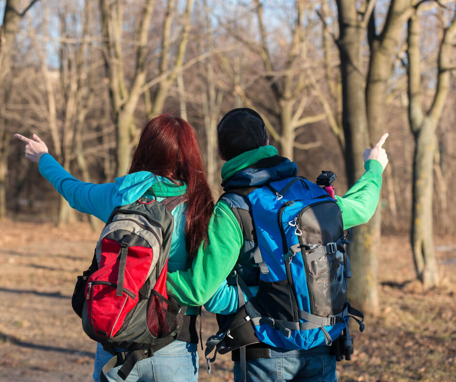 Two backpacked teens gesturing towards something off-screen, appearing curious and engaged.