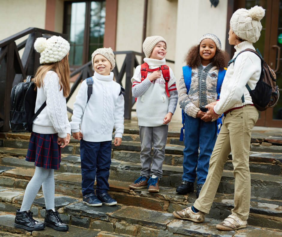 A group of children with backpacks standing together on steps, smiling and chatting