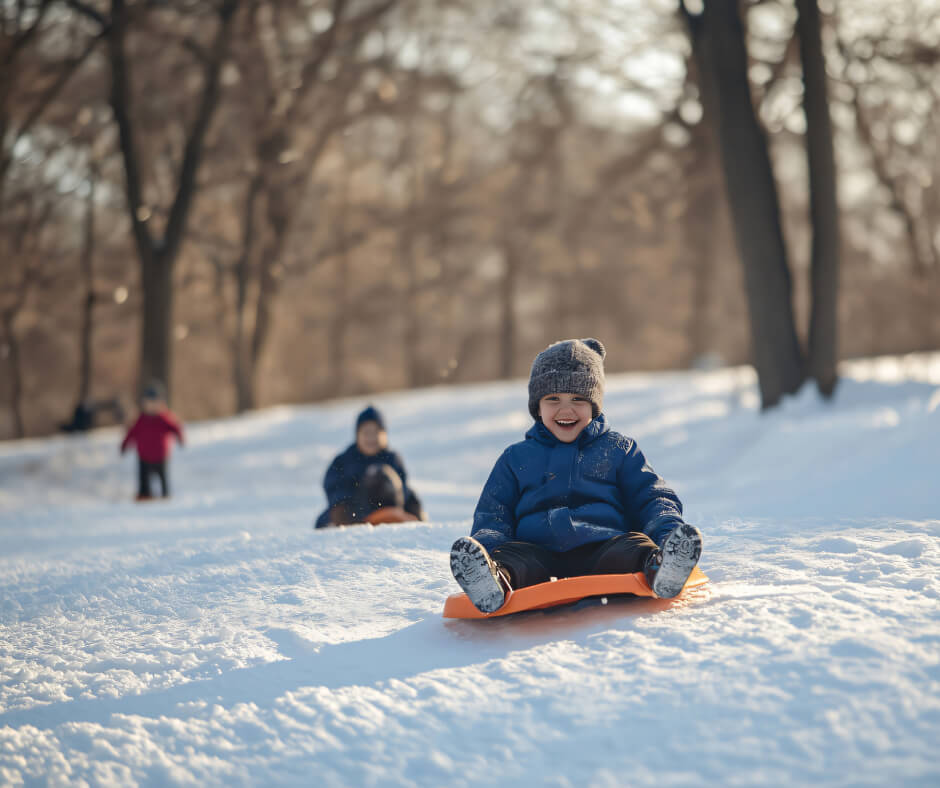 A young boy joyfully rides a sled down a snowy hill, surrounded by a winter landscape.
