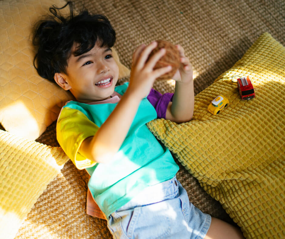 A young boy reclines on a couch, focused on a toy car in his hands, surrounded by a cozy living room.