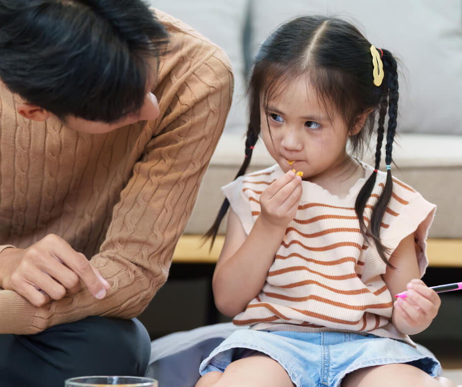 A father and a little girl are seated on the floor, each holding a toothbrush, sharing a moment of dental care together.