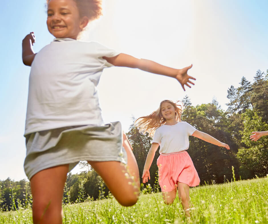 children joyfully running through a green field under a clear blue sky