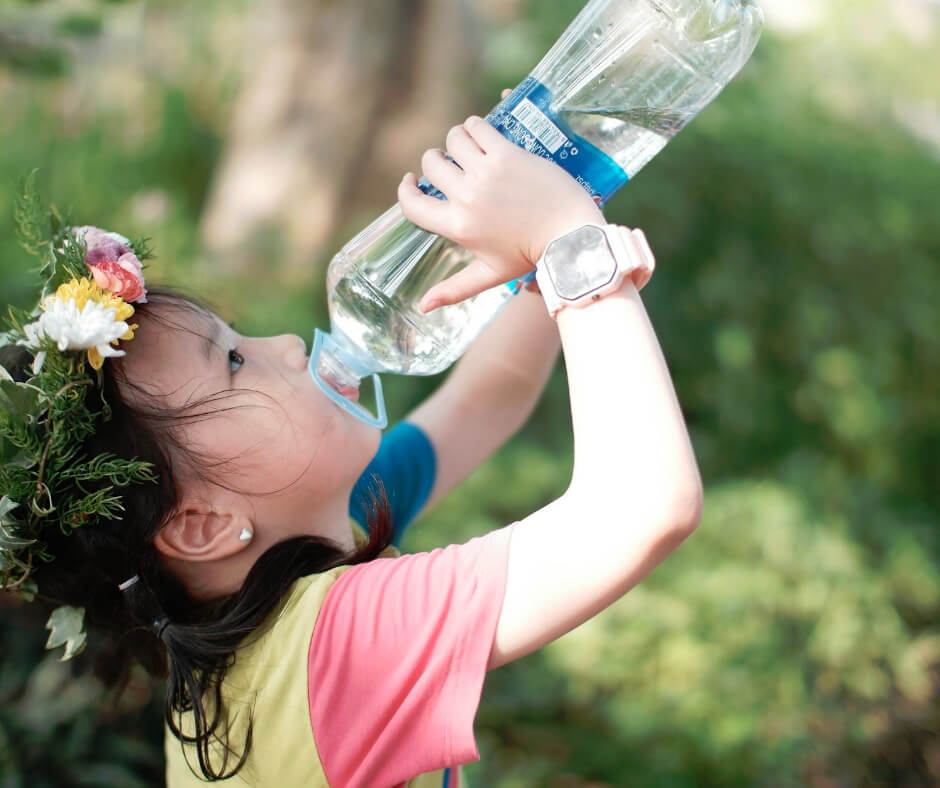 Young girl drinking water from bottle outdoors with flower crown supporting healthy immune system during seasonal changes