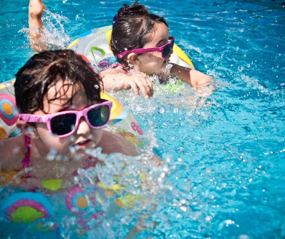 Two kids wearing sunglasses swimming with floaties in a pool, illustrating summer water safety for children