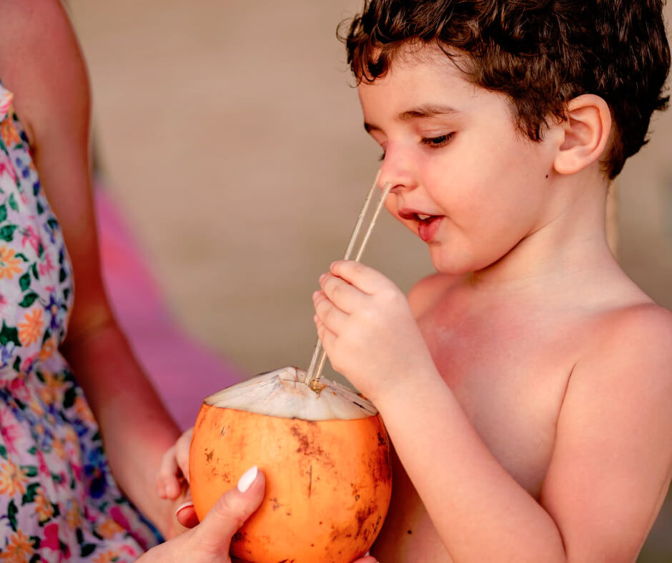 Young child drinking fresh coconut water through a straw, a healthy summer hydration option for kids