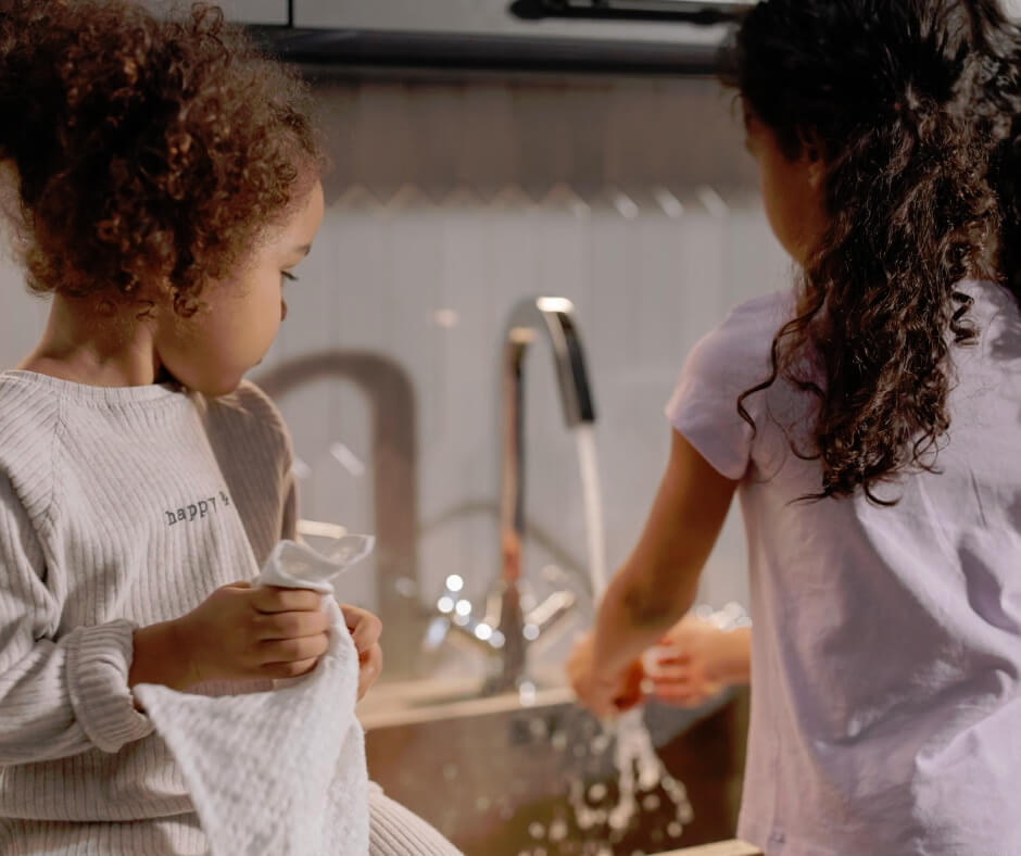 Two young girls washing dishes together at kitchen sink, teaching kids responsibility through age-appropriate chores