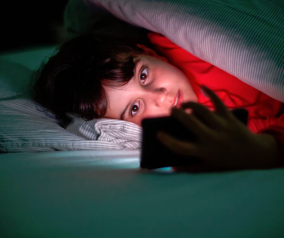 Child hiding under blanket at night using smartphone, illustrating screen time effects on children's sleep health