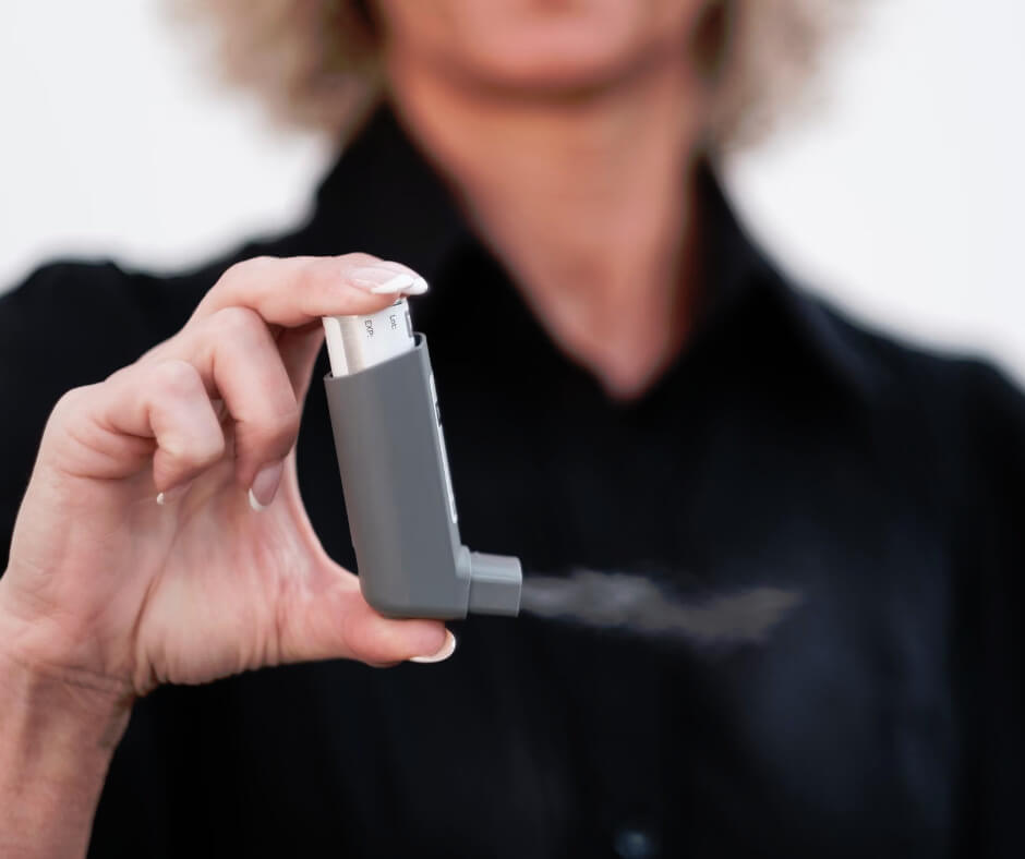 Woman holding gray metered-dose inhaler releasing medication mist, illustrating childhood asthma treatment options for kids