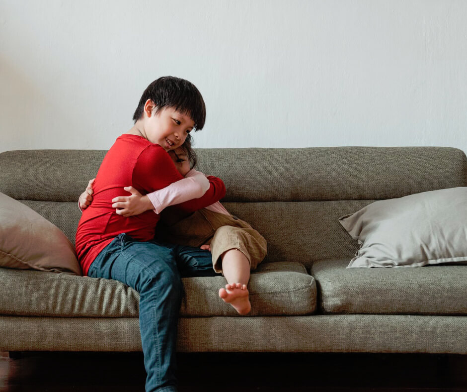Two young siblings hugging warmly on a couch, showing sibling connection and appreciation in a cozy home setting
